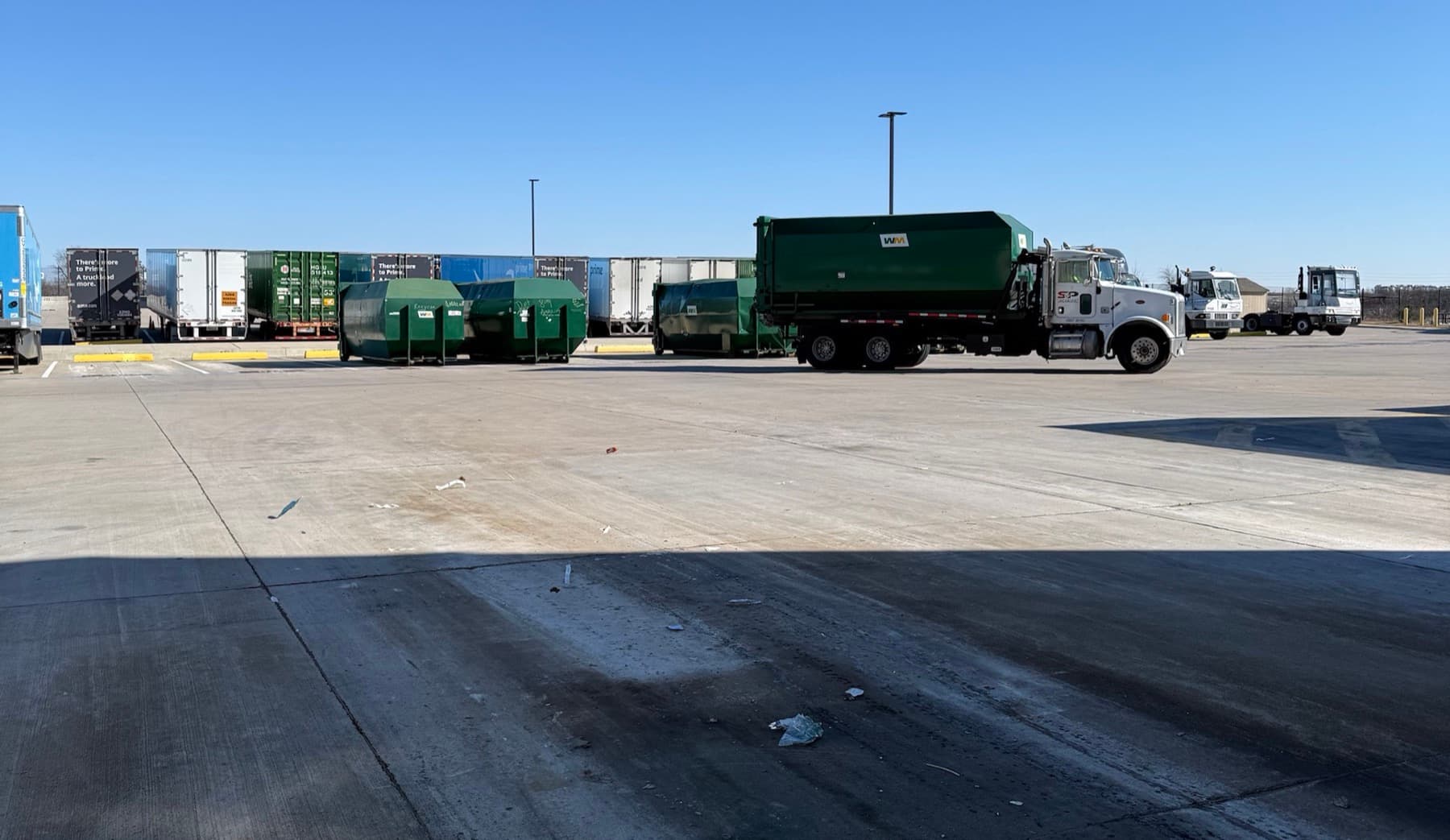 An S&P Dumpsters truck with a loaded compactor box on the back, alongside a row of compactors at a Central Texas distribution yard