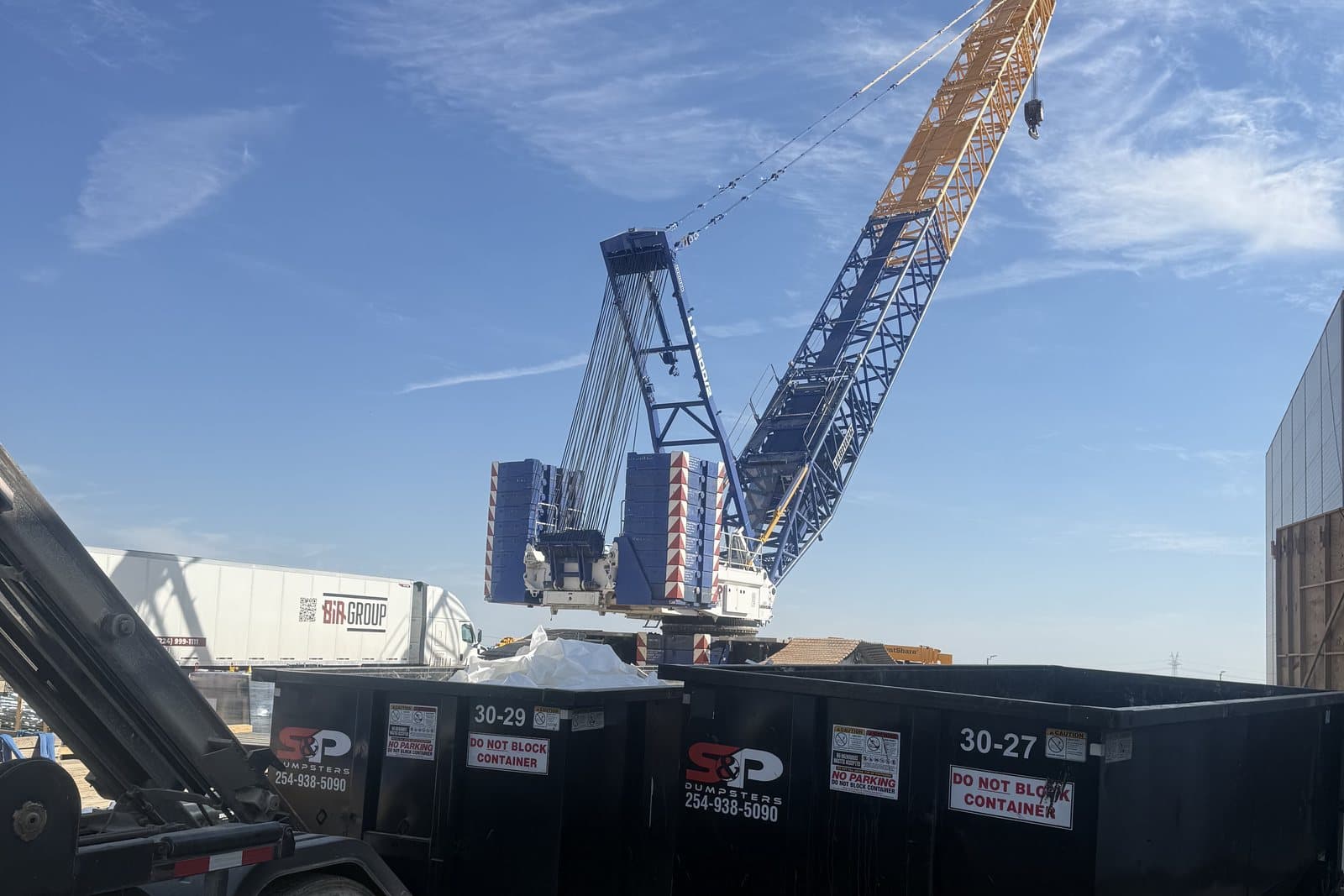Two S&P roll-off containers staged beside a crawler crane on a Central Texas data centre construction site