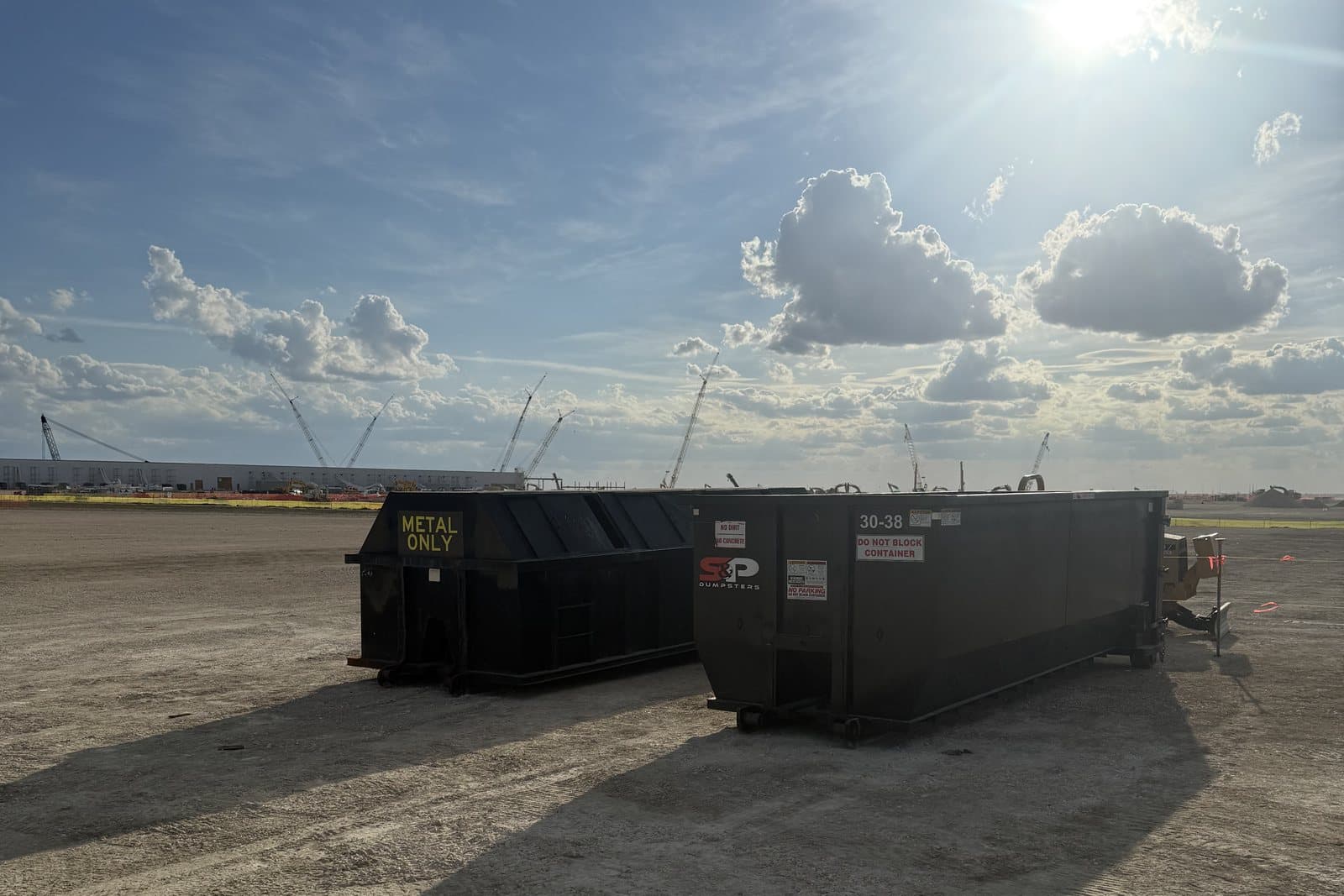 An S&P metal-only container beside a 30 yard roll-off on a large open Central Texas construction site