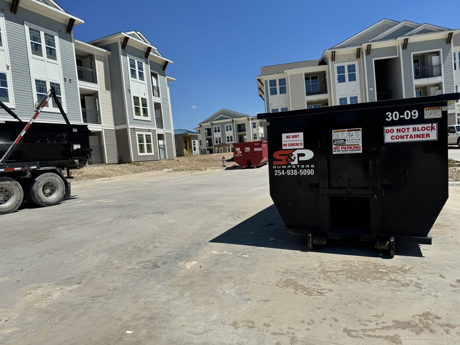 An S&P roll-off truck and two 30 yard containers staged between buildings at an apartment complex under construction
