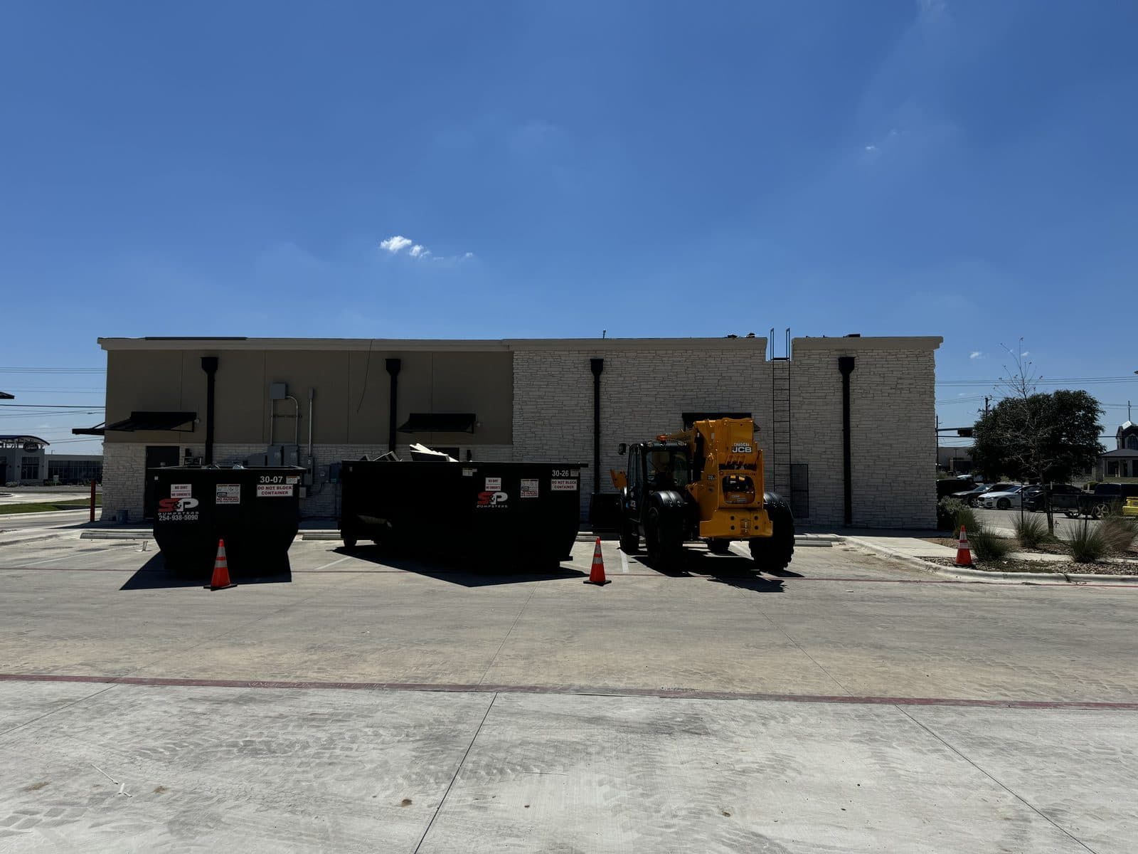 Two S&P 30 yard containers and a telehandler at a commercial building during a re-roof