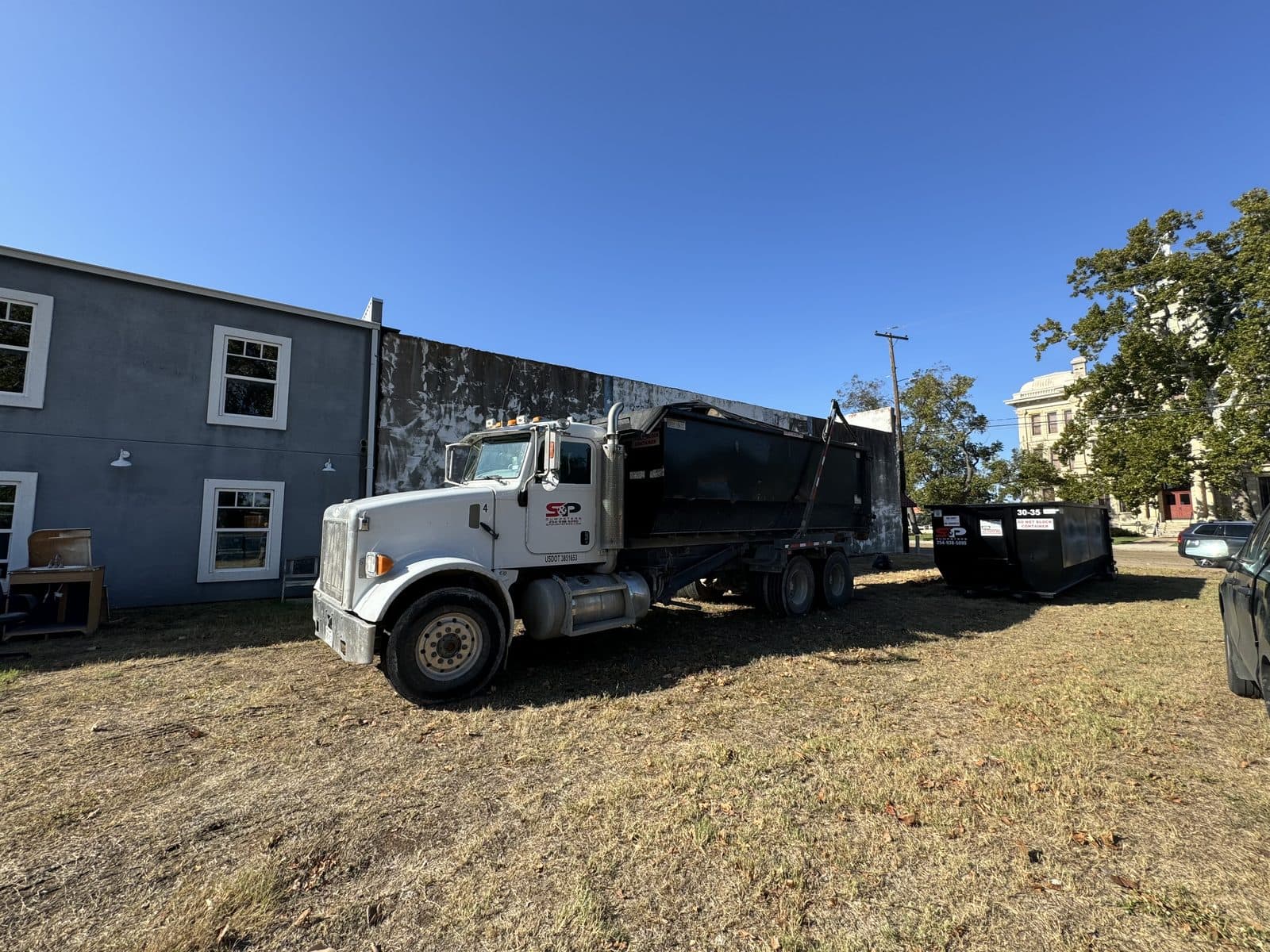 An S&P truck loading a full 30 yard container while a second empty container already sits in place on a downtown Cameron remodel