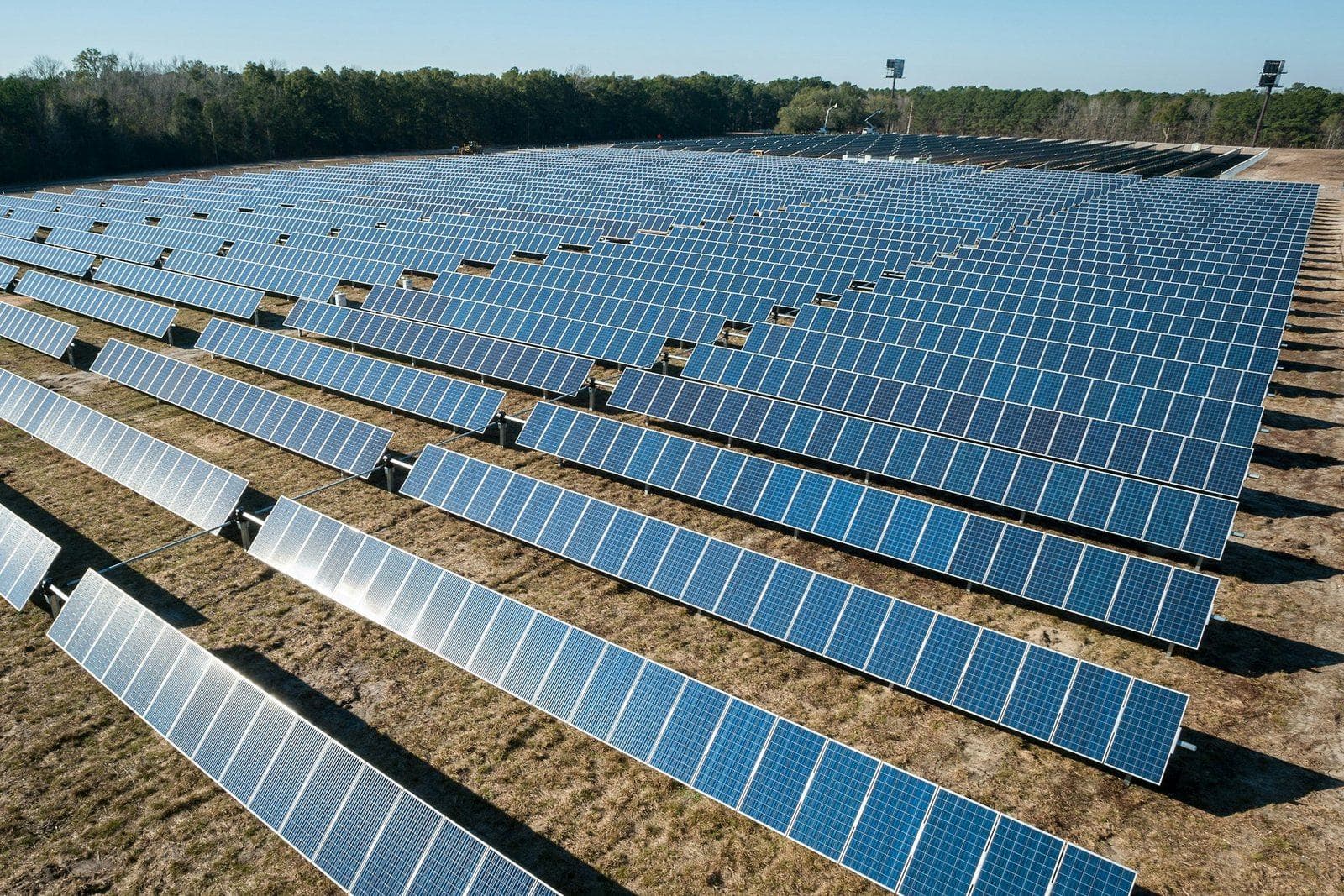 Rows of solar panels across a utility-scale solar farm on dry open ground